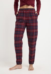 Pantalones de pijama de cuadros rojos y azul marino hechos de una tela suave, con una cinturilla elástica, bolsillos laterales y puños ajustados en los tobillos.
