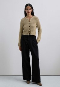 Cárdigan de punto beige con un patrón texturizado, con botones negros y un corte corto, combinado con pantalones anchos de tiro alto en negro.