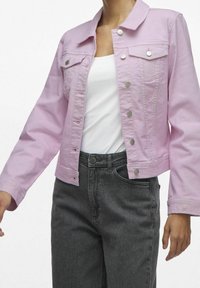 Chaqueta de mezclilla rosa claro con un diseño corto, botones de presión metálicos y dos bolsillos en el pecho, combinada con unos jeans grises de cintura alta.