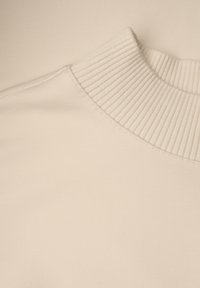 Kremowy prążkowany kołnierz z gładkiego, miękkiego materiału, prezentujący neutralny kolor i bezszwowy design.