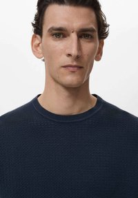 Maglione strutturato blu navy con scollo a girocollo e polsini a coste, caratterizzato da un motivo intrecciato. Il tessuto appare morbido e flessibile.