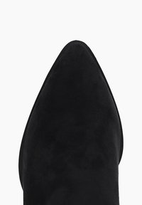 Chaussure noire en suède à bout pointu avec une texture lisse et une semelle plate, arborant un design épuré sans quincaillerie ou motifs visibles.
