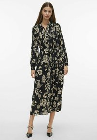 Robe portefeuille noire à motifs floraux avec des manches longues, mettant en avant des imprimés botaniques de couleur claire, une ceinture à nouer à la taille et une jupe de longueur intermédiaire.