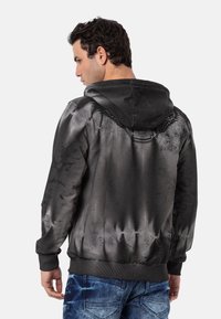 Sweat à capuche noir dégradé avec une finition texturée, présentant un logo dans le dos et des poignets et ourlet côtelés, porté avec un jean bleu.