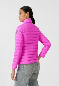 Giacca imbottita rosa con cuciture orizzontali, collo alto e toppa con logo sulla manica. Indossata con jeans grigio chiaro, che mette in risalto una silhouette aderente.