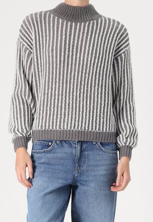 Person wearing a gray and white vertically striped knit sweater with ribbed collar, cuffs, and hem paired with blue jeans.