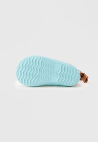 Semelle de chaussure en caoutchouc bleu clair avec un motif en zigzag ; présente une sangle en cuir marron attachée. Texture lisse avec une forme arrondie.