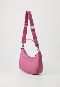 Small textured pink leather handbag with gold zipper, short handle, and adjustable wide fabric shoulder strap with logo text.