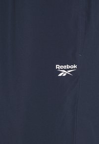 Calções de desporto azul marinho feitos de um tecido leve, apresentando um logótipo branco da Reebok na parte inferior e detalhes de costura subtis.