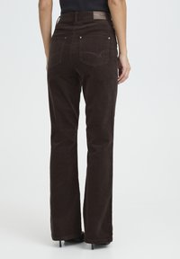 Brown corduroy flared pants with a high waist, featuring back pockets and a branded label at the waistband. Smooth texture and subtle sheen.