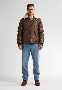 Bruine leren jas met een beige schapenvachtkraag, rits aan de voorkant, zijzakken en logodetail. Gecoordineerd met lichtblauwe spijkerbroek en bruine laarzen.