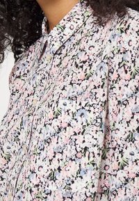 Chemise à boutons florale avec un fond noir et des motifs floraux roses, bleus et verts, à manches longues et col classique.