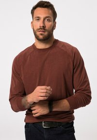 Bordeauxrotes Langarm-Sweatshirt mit Rundhalsausschnitt, gerippten Bündchen und lockerer Passform, kombiniert mit dunklen Jeans und einem schwarzen Gürtel.