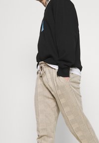 Svart sweatshirt med rund halsringning, tillsammans med ljusbeige rutiga byxor med elastisk midja och sidofickor.