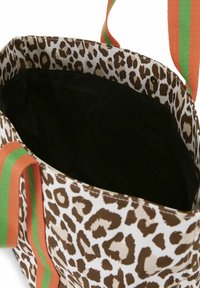 Torba na ramię w panterkę w kolorach brązu i kremu, z pomarańczowymi i zielonymi paskami oraz czarną podszewką.