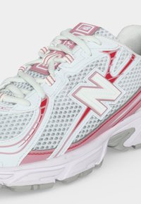 Άσπρο και ροζ αθλητικό παπούτσι New Balance για τρέξιμο με πλέγμα στην επάνω επιφάνεια, κλείσιμο με κορδόνια και παχιά μαλακή σόλα, εμφανιζόμενο από πλάγια γωνία.
