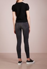 Czarna bluzka z bufiastymi rękawami zestawiona z wysokimi, ciemnoszarymi skinny jeansami oraz czarnymi sneakersami z białymi podeszwami. Miękki, dopasowany materiał.