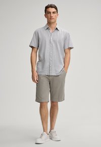 Lichtgrijs kortemouwen shirt met knopen, gecombineerd met lichtgrijze shorts met een gestructureerd patroon en witte sneakers.