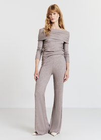 Geripptes, schulterfreies Oberteil mit langen Ärmeln in weichem Taupe, kombiniert mit ausgestellten passenden Hosen. Beide haben eine strukturierte Strickoptik mit enganliegender Passform.
