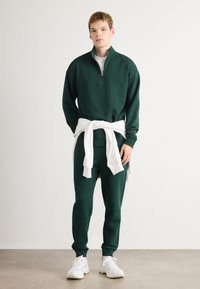 Felpa nera con zip e colletto alto, abbinata a pantaloni sportivi a gamba affusolata dello stesso colore. Una felpa bianca legata in vita. Sneakers bianche.