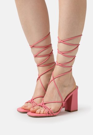 Sandalias de tacón rosa con un tacón bloque y diseño de tiras entrecruzadas que se envuelven alrededor del tobillo. Fabricadas con un material suave y flexible.