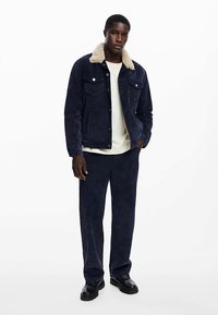 Navyblå jeansjacka med beige fuskfårskinnskrage, fickor framtill och matchande marinblå manchesterbyxor. Svarta skor fullbordar outfiten.