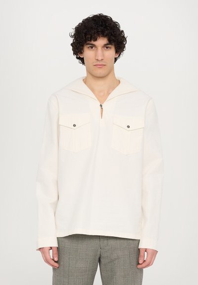 Chemise à manches longues crème clair avec capuche, dotée d'une patte de boutonnage quart, de deux poches poitrine et d'une coupe décontractée, associée à un pantalon à carreaux.