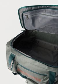 Ανοιχτή γκρι και τιρκουάζ τσάντα duffel Patagonia που δείχνει το άδειο κύριο διαμέρισμα και την τσέπη με φερμουάρ από δίχτυ στην επάνω πτυχή.