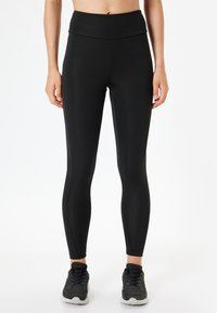 Svarta tights gjorda av elastiskt tyg med hög midja och avsmalnande ben, med en slät yta och minimala sömdetaljer.