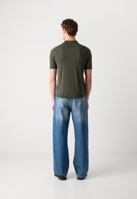 Olivengrønn polo-skjorte med korte ermer kombinert med brede lys blå denimjeans, som viser en jevn tekstur og uformell passform.