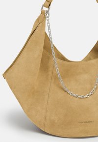 Wildleder-Umhängetasche in Hellbraun mit geschwungener, Hobo-Form. Verfügt über eine silberne Kettenakzentuierung und den eingeprägten Markennamen an der Seite.