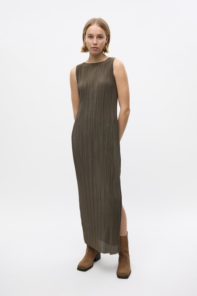 Langes, olivengrünes, plissiertes Kleid mit hohem Ausschnitt und seitlichem Schlitz, kombiniert mit braunen Stiefeletten. Glatte Textur und lässige Passform.