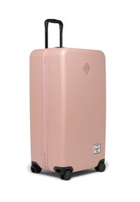 Roze tvrdi kofer s glatkom površinom, crnim produžnim ručkom, četiri kotača i logom na prednjoj strani.