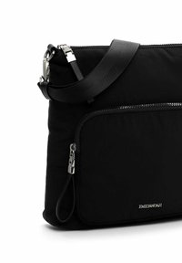Black nylon shoulder bag with a textured surface, featuring a front zip pocket, silver hardware, and a detachable strap.