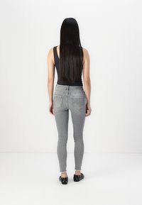 Jean skinny gris avec une taille mi-haute, cinq poches et un léger délavage. Associés à des chaussures noires à enfiler, vus de dos.