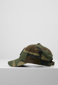 Camouflage baseball cap in various shades of green and brown. Features a curved brim, adjustable strap, and embroidered logo detail.