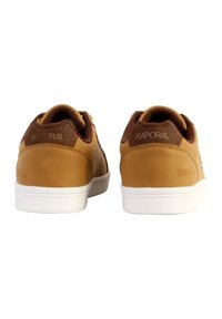 Baskets en cuir tan avec des accents marron et des semelles en caoutchouc blanches. Présente un logo sur le talon et des détails texturés sur le côté.
