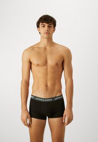 Fekete férfi boxer alsónadrág, puha elasztikus derékpánttal, amelyen a "JACK & JONES" márkaneve kontrasztos kék-szürke színben látható. Egyszerű, testhezálló kialakítás.