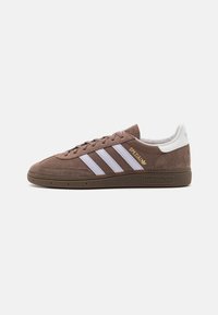 Bruna Adidas-sneakers med vita ränder, "Spezial"-text i guld, mockatå med texturerad gummisula, visad från sidan på en vit bakgrund.