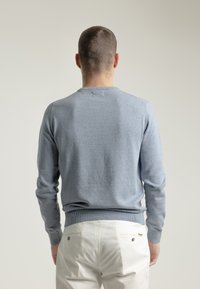 Suéter azul claro hecho de una tela suave, con un escote redondo y puños de canalé. La vista trasera muestra una superficie lisa y sin adornos.