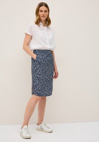 Une jupe marine avec des motifs de feuilles blanches, dotée de poches et de fentes sur les côtés. Associée à une chemise blanche à boutons et des baskets légères.