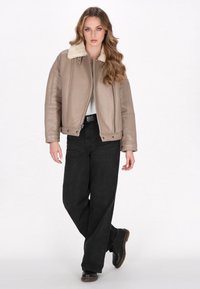 Giacca in pelle beige con colletto in shearling a contrasto, chiusura con zip e accessori in argento, abbinata a pantaloni neri a gamba larga e stivali neri.