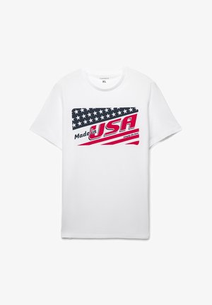 Biała bawełniana koszulka z grafiką przedstawiającą flagę Stanów Zjednoczonych, napis "Made in USA", czerwoną i niebieską kolorystyką oraz casualowym krojem.