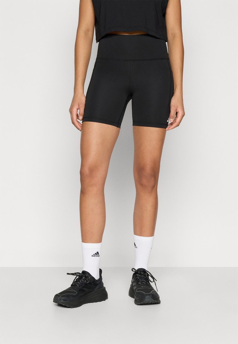 Crne sportske kratke hlače od rastezljivog materijala, s visokim strukom i uskim krojem. Nošene s crnim tenisicama i bijelim čarapama.