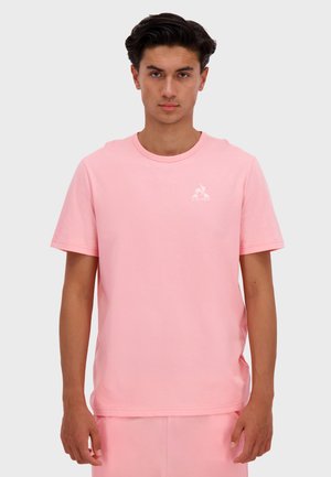Pink cotton t-shirt with short sleeves and a round neck. Features a small white logo on the left chest area. Smooth texture.