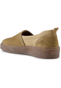 Bruna mockaskor i slip-on-modell med ett ljusbrunt elastiskt band, med en texturerad korksula och en liten etikett på sidan.