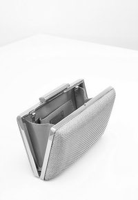 Rektangulær sølvclutch med tekstureret overflade, åbnet for at afsløre grå stofindvendig og lille indvendig lomme, placeret på en hvid overflade.