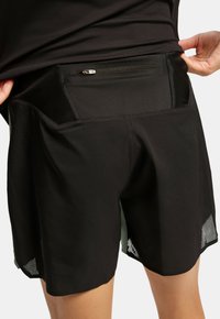 Shorts deportivos negros hechos de material texturizado, con un bolsillo trasero con cremallera y acentos de malla en el dobladillo para mayor transpirabilidad.