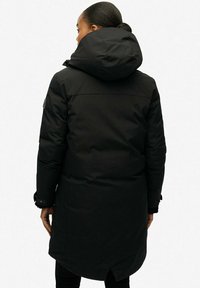 Czarna kurtka puchowa z dużym kapturem, długim fasonem i teksturowanym materiałem. Zauważalne szczegóły to rozcięty dół i regulowane mankiety.