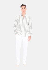 Camicia a righe verde e bianca con colletto button-down, maniche lunghe e vestibilità rilassata, abbinata a pantaloni bianchi e sneakers.